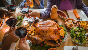 感恩节餐桌上放着烤火鸡，人们举起红酒酒杯。＂class=