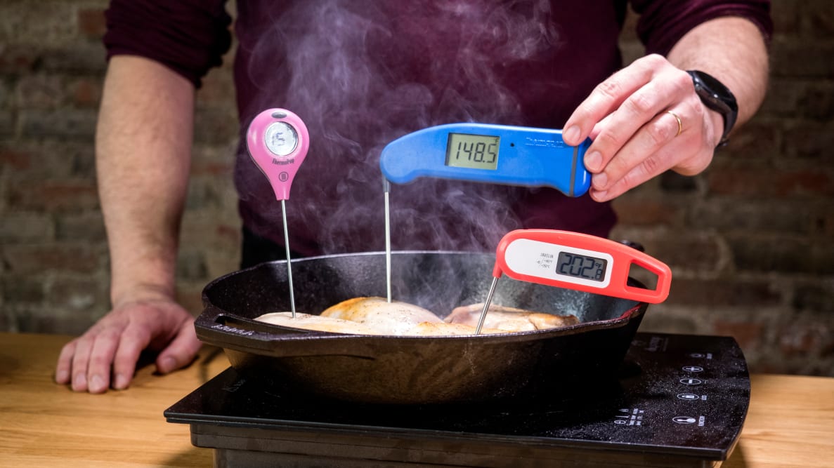Digital meat thermometers are used to measure chicken inside a cast-iron pan.