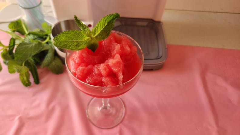 A coupe glass filled with a frozen cocktail with mint garnish in front of the Cuisinart Mix It In Soft Serve Ice Cream Maker.