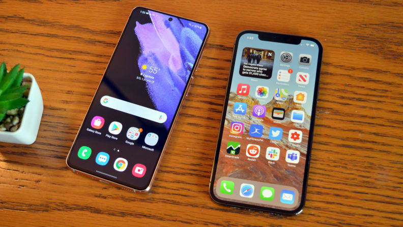 An Android phone and an iPhone resting next to each other on a wooden table, both showing their home screens.