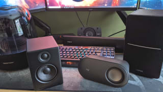 A pair of PC speakers on a desk with a monitor in front