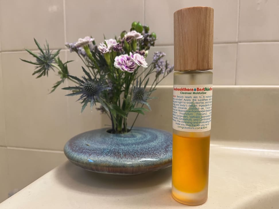 Living Libations Seabuckthorn Oil sits on a bathroom vanity in front of a floral arrangement.