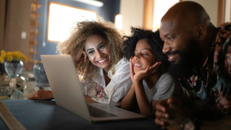 Family of three smiling at laptop.