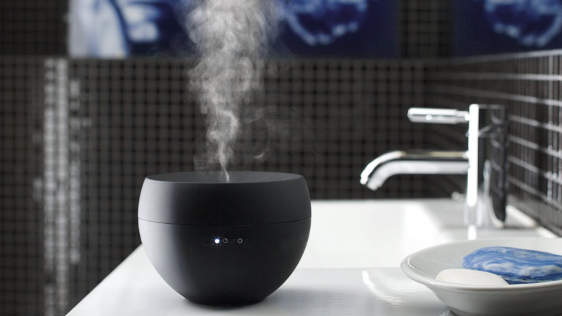 A black Stadler Form Jasmine essential oil diffuser sits on a bathroom sink.