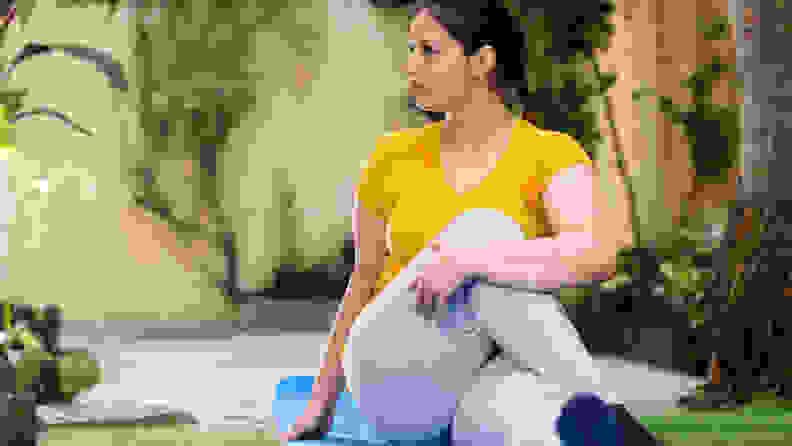 Outdoor image of Asian/ Indian woman doing morning exercise and yoga in garden on exercise mat. She is stretching her body which help ease back pain, flexible body and relief in mussels.