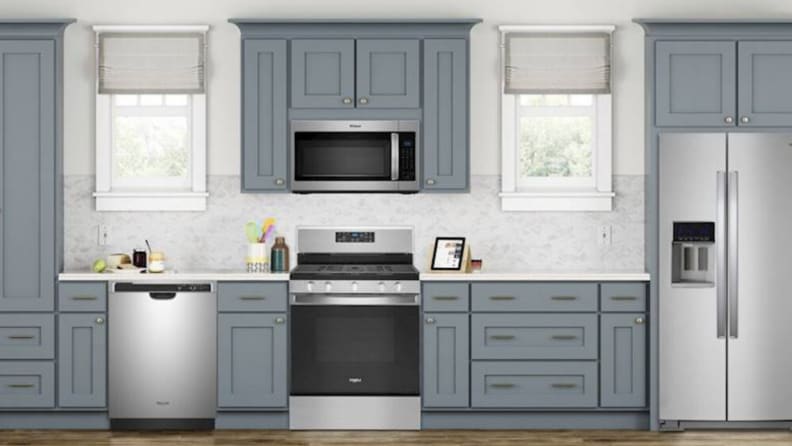 In the center of a modern kitchen with gray cabinetry and white background, a Whirlpool WFG525S0JS gas range is mounted just below a microwave.
