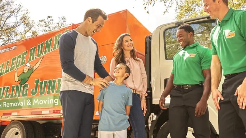 A family and two movers all smiling at each other in front of a hauling truck
