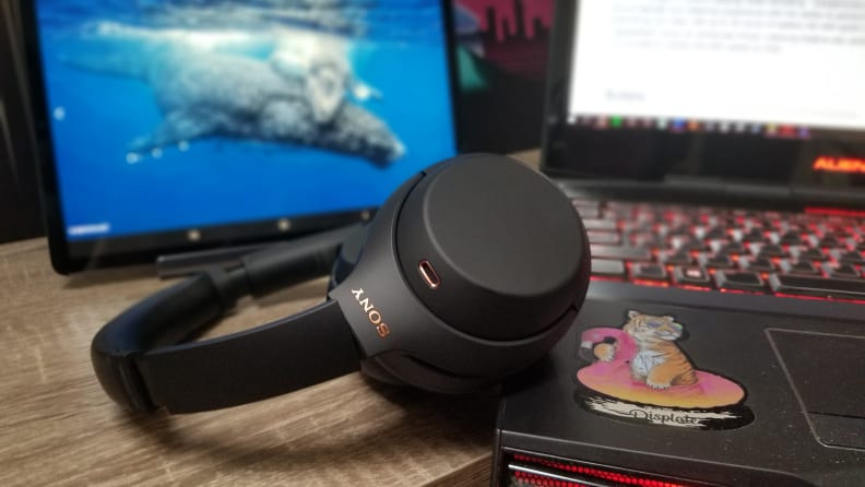 Black colored headphones on wooden desk next to open gaming laptop with colored keyboard.