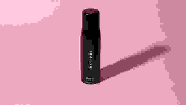 A black bottle of makeup setting spray on a pink background.
