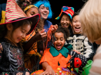 Happy children in different festive Halloween costumes at door collecting candy from bowl.