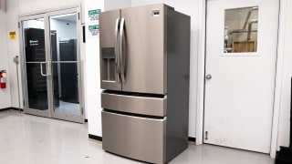A silver French-door refrigerator stands in a lab setting against a white wall
