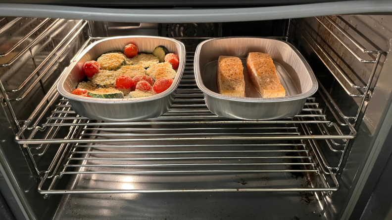 Two tins of veggies and salmon in an oven.