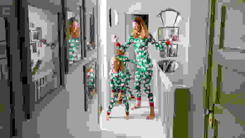 A mom and two children wearing matching green Christmas pajamas dancing in a hallway