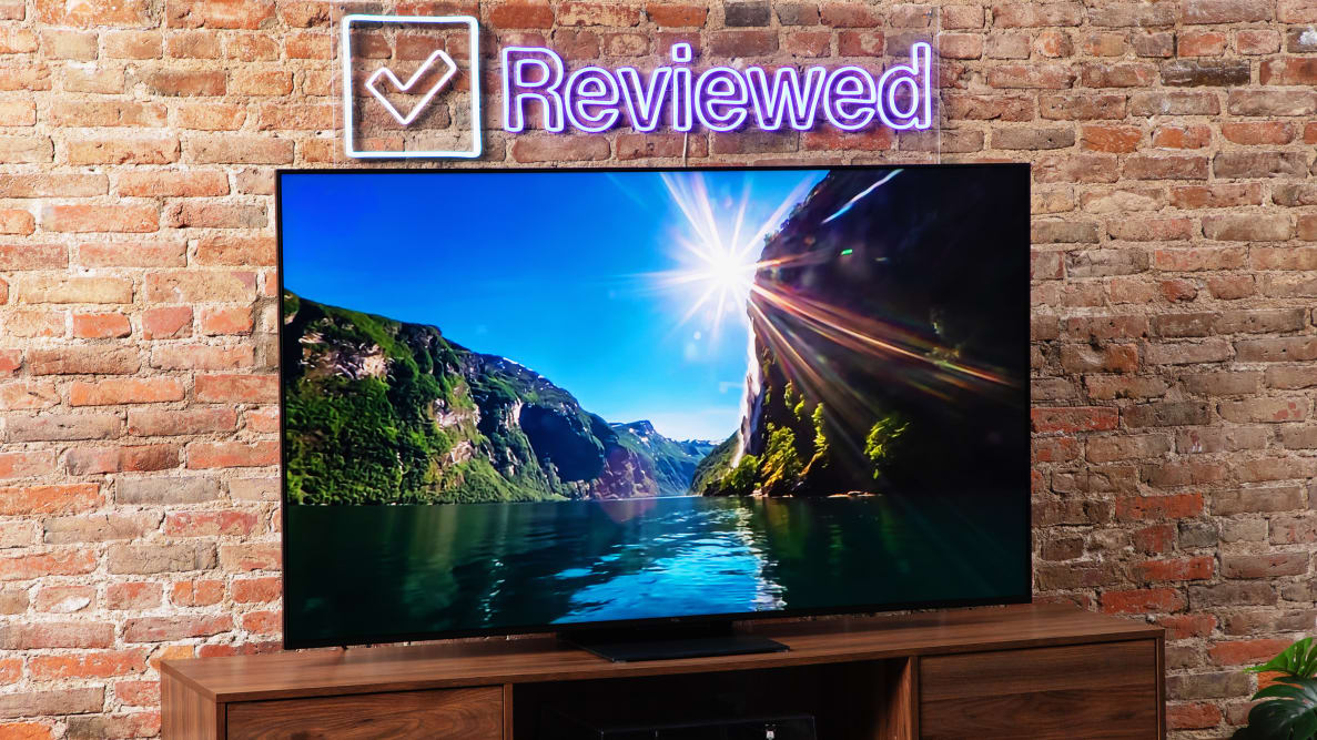 The TCL QM8 LED TV showing a vibrant canyon river onscreen in front of a brick background.