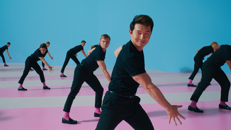 A still from the Barbie movie, featuring several Kens dancing on a pink, white, and blue background.
