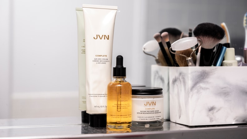 A cream colored squeeze tube and jar with a bottle of yellow hair oil sitting on a vanity.