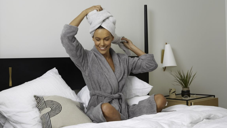Women sitting in grey bathrobe on bed with white comforter