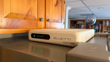 Bluetti FridgePower shown on top of a silver refrigerator in front of wooden cabinets, with a disco ball hanging from the ceiling in the basement shown in the background.