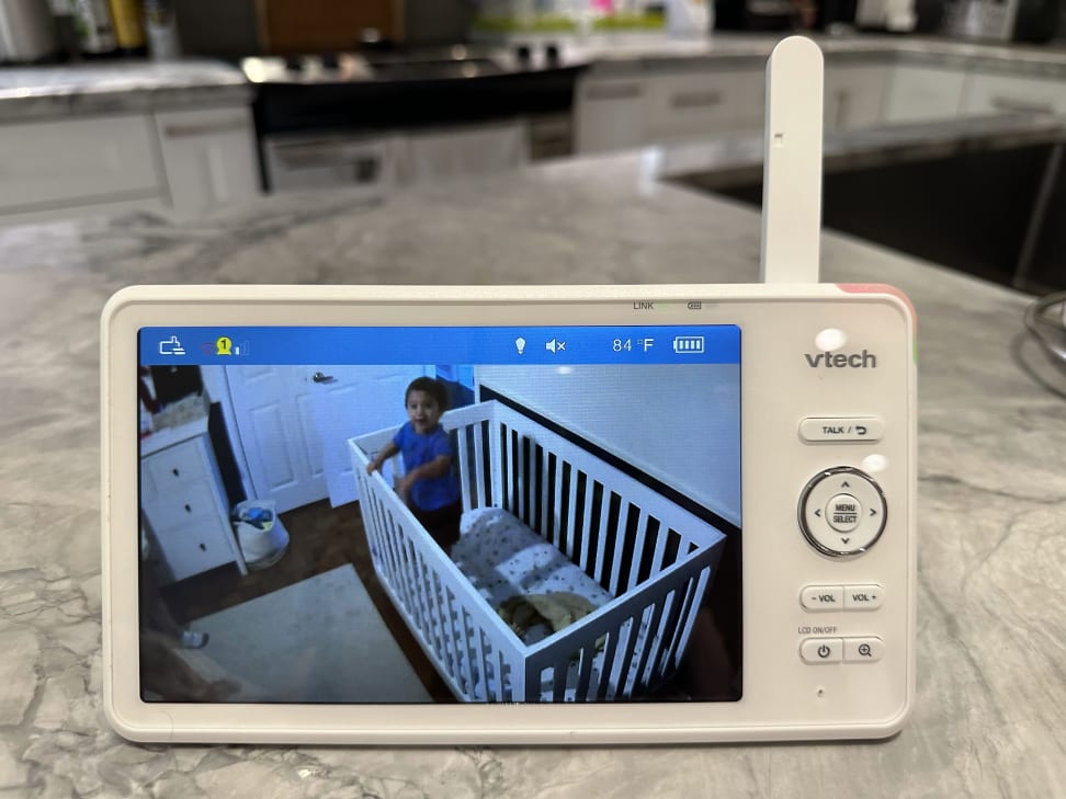 A Vtech baby monitor on a kitchen counter displays a child in a crib on its screen.