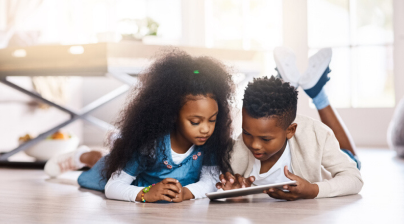 Two kids lay on the floor and play on their tablet