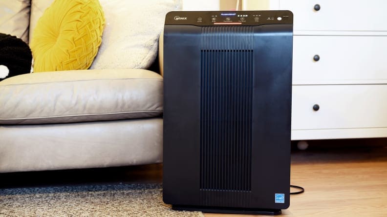 A black Winix air purifier sits at the edge of a beige leather couch.