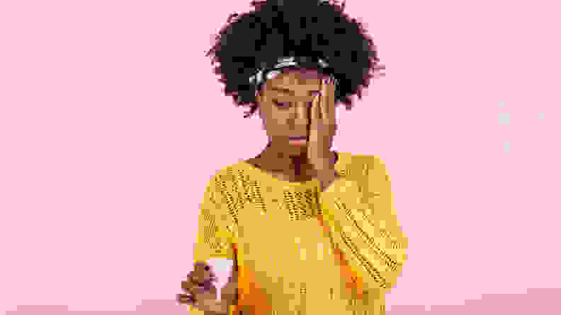 沉思的非裔美国女性拿着有效安全实惠的月经用品，很好的防止渗漏，选择可重复使用的月经杯，思考如何使用，在粉红色的墙上留空