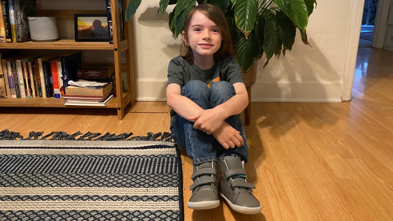 A smiling child wearing Ten Little shoes in grey high tops.