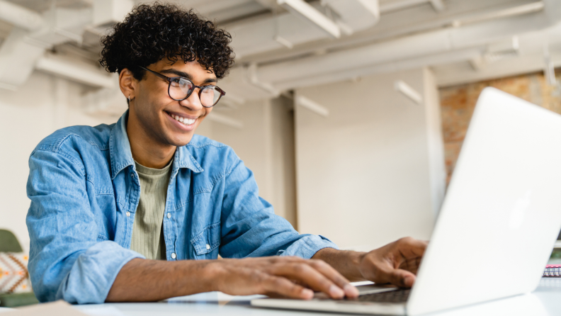 Person smiling while working on laptop on desk.