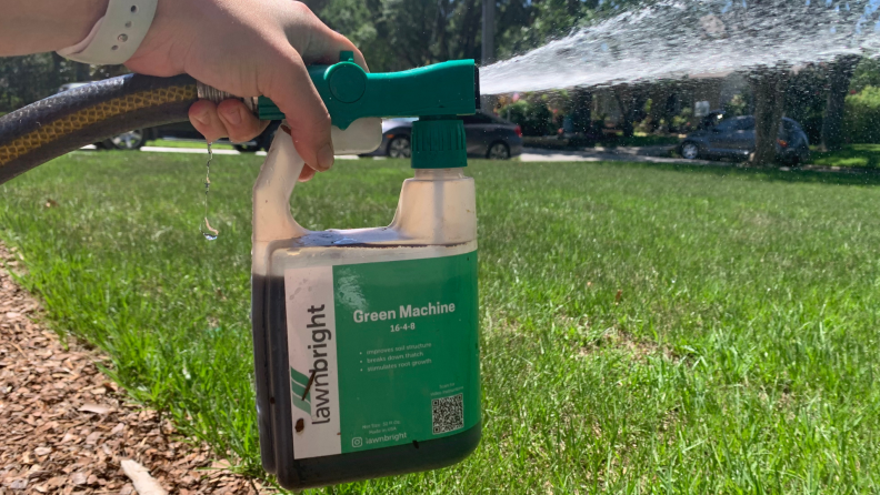 A bottle of liquid lawn fertilizer is attached to a garden hose and sprayed on the grass.
