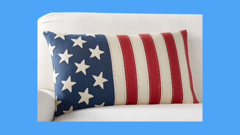 An American flag pillow on a white couch against a blue background.