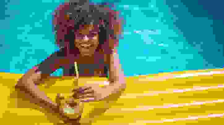 Person holding a drink on a yellow float in a pool
