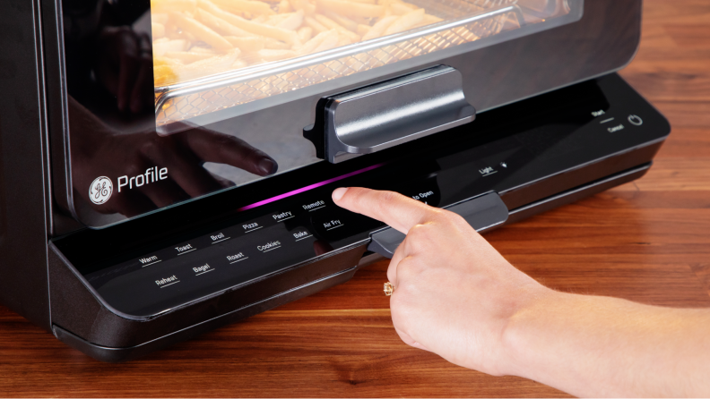 A hand pressing buttons on the GE Profile smart oven's interface.