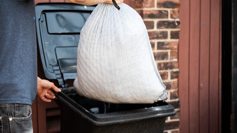 A person throwing a trash bag into a trash bin.