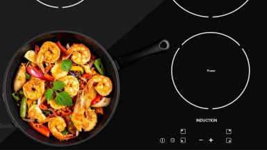 A cast-iron frying pan with shrimp and vegetables sits on an induction stovetop