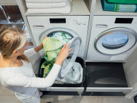 A person puts daily washing into the washing machine.
