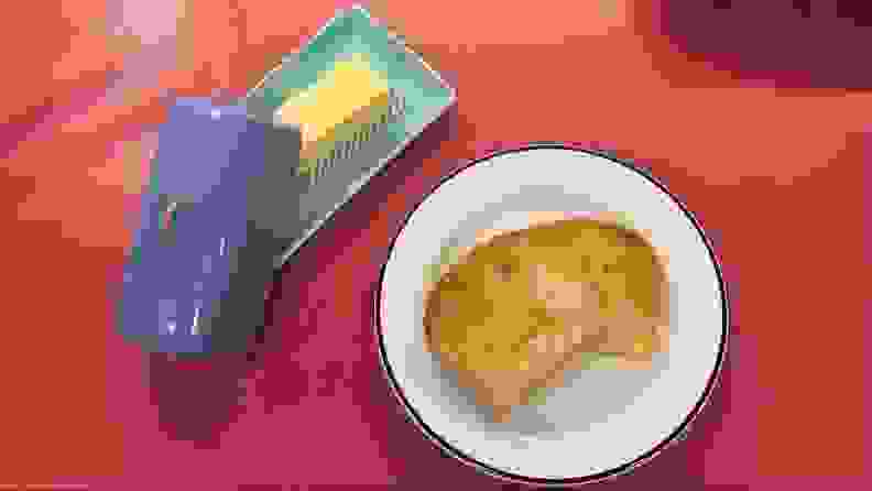 A white plate with a piece of toast on it, next to a blue glass tray with a stick of butter on it.