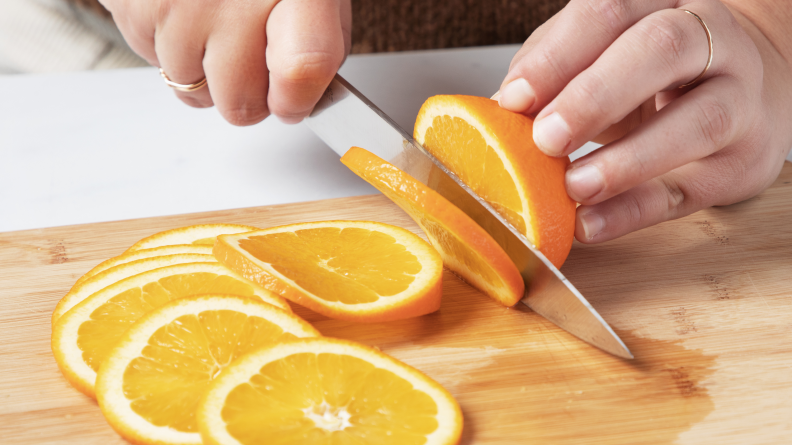 A person slicing oranges into rounds.