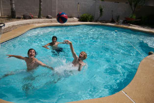 Three youths play pool basketball in an in-ground swimming pool.