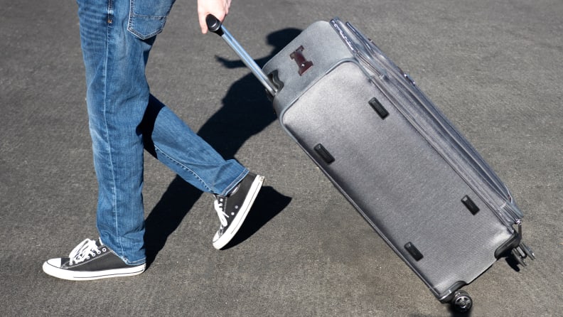 A wheeled suitcase is pulled across a paved street