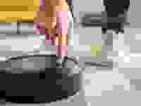 Cropped view of man pointing with finger at robotic vacuum cleaner in living room.