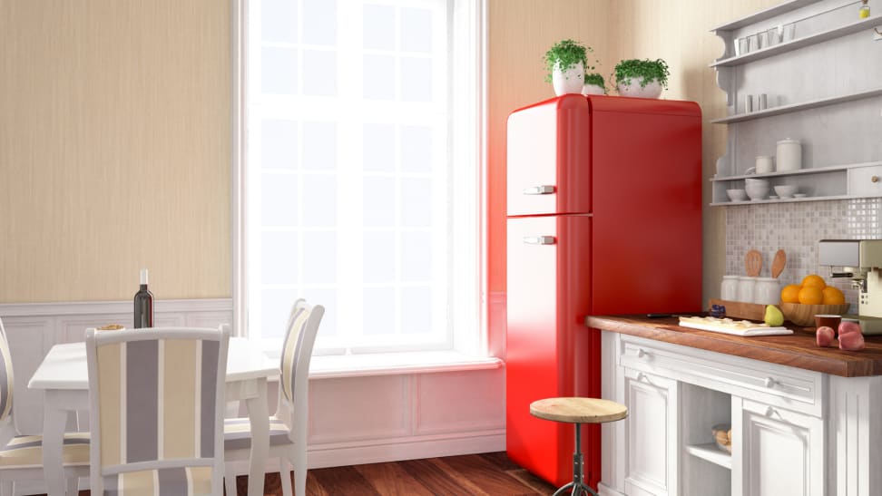 A brightly lit kitchen with a bright red fridge with plants on top.