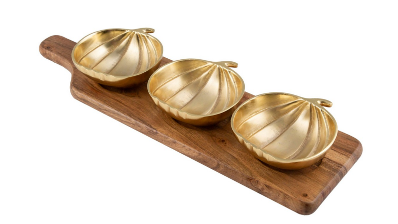 A wooden paddle board hosts three golden bowls in the shape of pumpkins.