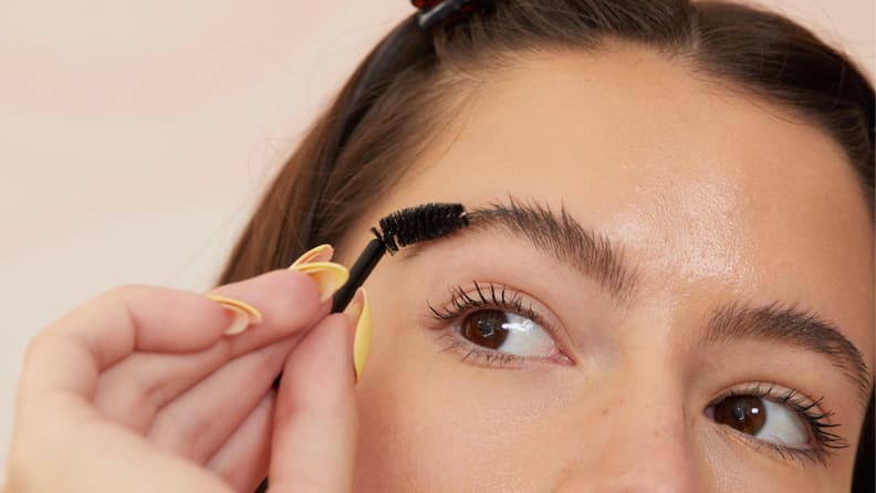 A closeup on the top half of a model's face as they hold a spoolie up to their eyebrow.