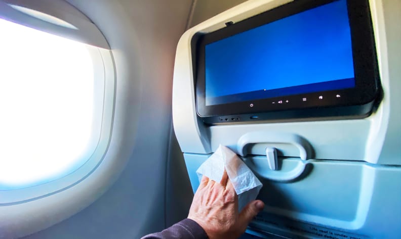 passenger wiping down airplane tray table with sanitizing wipe during covid-19 pandemic