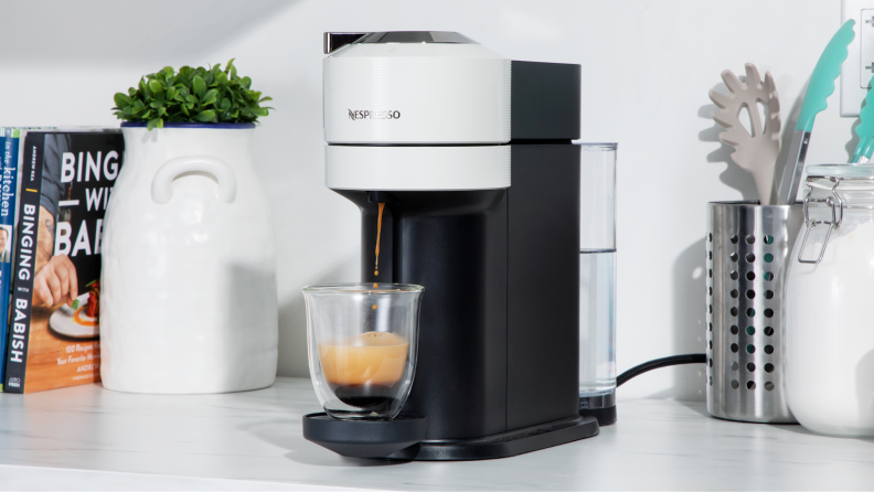 Nespresso Vertuo Next coffee maker on marble countertop next to potted plant and kitchen utensils.