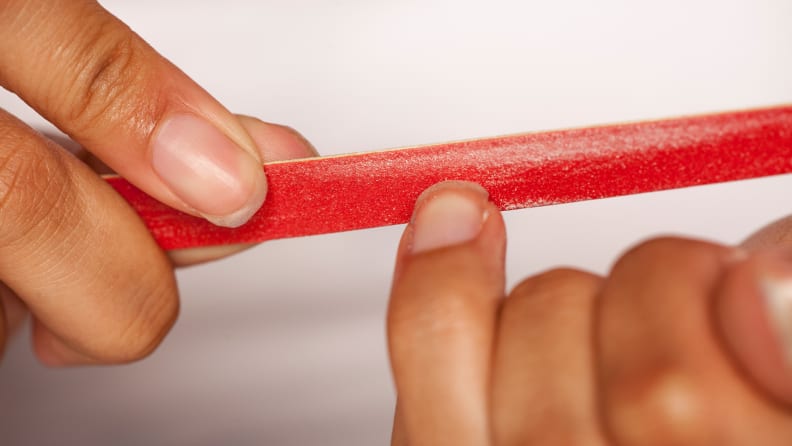 A closeup on a person's fingernail being filed by a nail file.