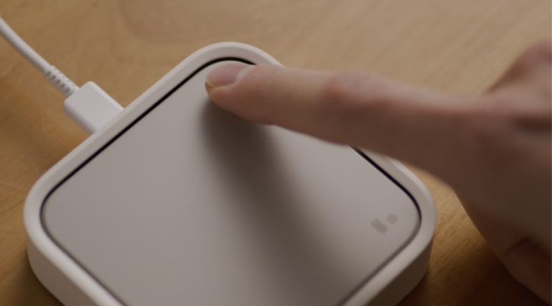 A finger pressing down on a smart home hub.