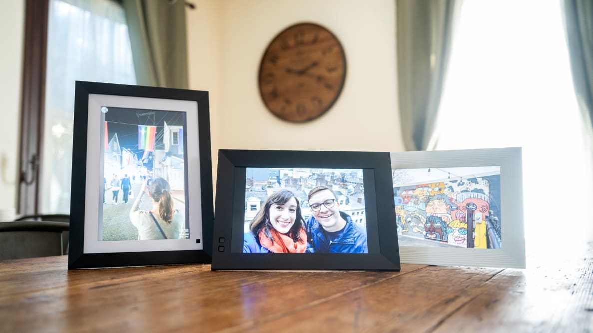 三个展示家庭照片的数码相框放在一张木桌上。