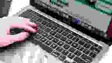 A pair of hands with painted fingernails type on a laptop keyboard