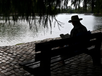 A person in a hat reads a book at the Regatas Lake in Buenos Aires.